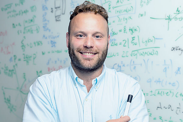 Darryl Seligman holding a marker standing in front of a whiteboard with equations on it.