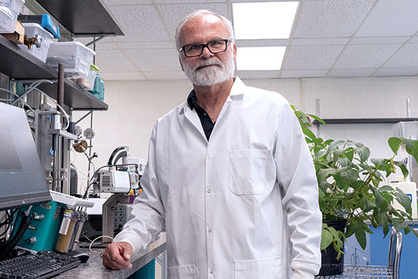 Tom Sharkey in the lab looking at the camera wearing a lab coat.