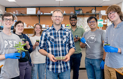 A male professor is surrounded by 4 male students and 2 female students in a lab.