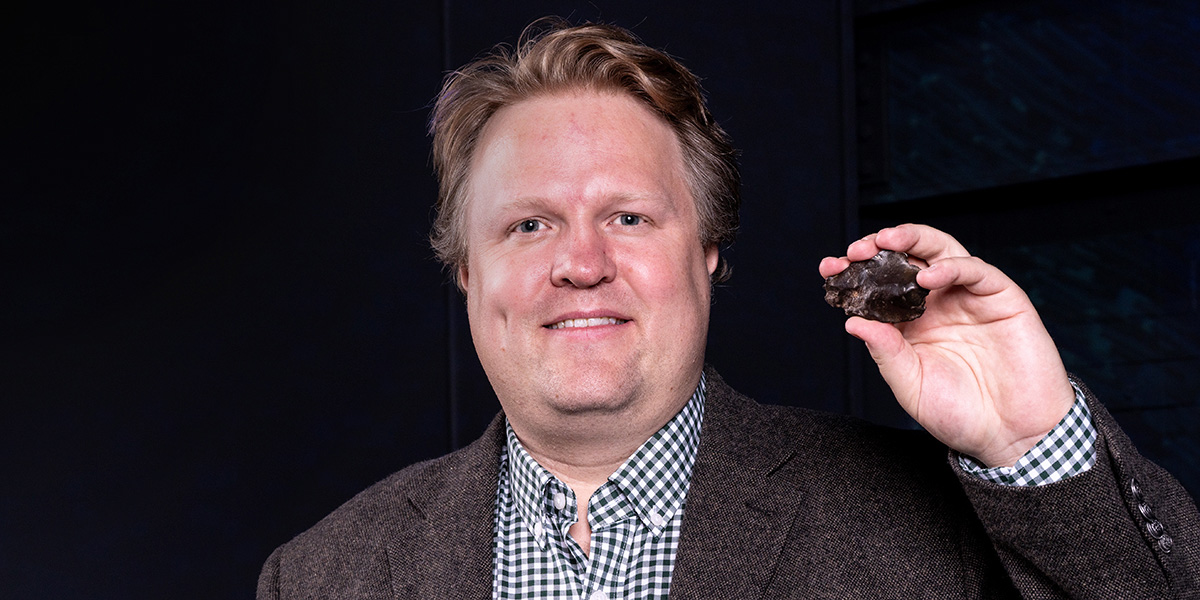 Seth Jacobson standing with a chunk of asteroid in his right hand.
